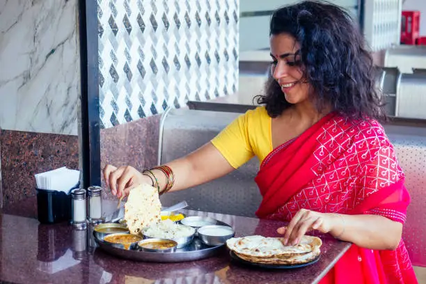 beautiful brunette woman in red sari eating with appetite traditional thali wirh rise,curd,dal in Goa restaurant masala tea.