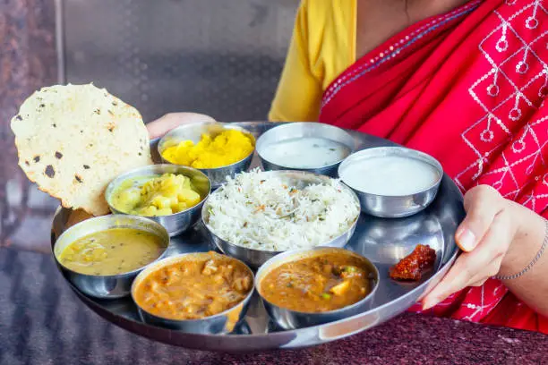 Photo of beautiful brunette woman in red sari eating with appetite traditional thali wirh rise,curd,dal in Goa restaurant masala tea