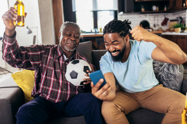 Man with senior father support favorite sports team together use smartphone app to online bet stock photo