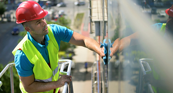 Side view of a mid 30's man washing windows on a residential building facade.