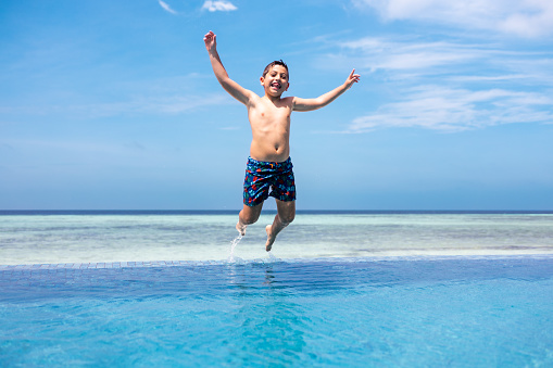 Funny kid jumping into a infinity swimming pool
