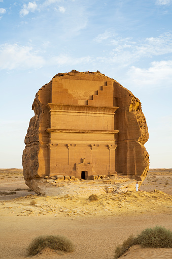 Middle Eastern man providing sense of scale for massive tomb of Lihyan, son of Kuza, erected in 1st-century CE and UNESCO World Heritage Site.