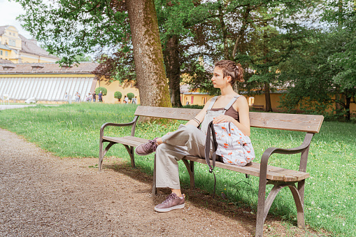 young beautiful teenager girl, with hair tied in bun, with oyukzak, sits on park bench. Beautiful girl outdoors on summer day. nature background.