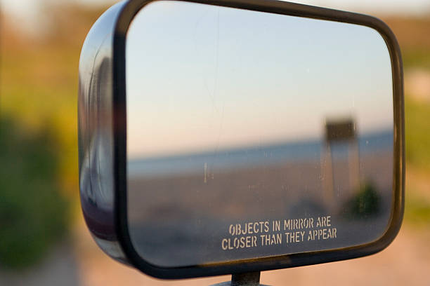 Side view mirror with legend OBJECTS IN MIRROR ARE CLOSER. Beach reflection through the rear view mirror mirror object stock pictures, royalty-free photos & images