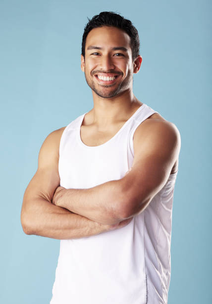 istock Handsome young hispanic man posing in studio isolated against a blue background. Mixed race male athlete wearing a vest and looking confident, healthy and fit. Exercising to increase his strength 1398977222