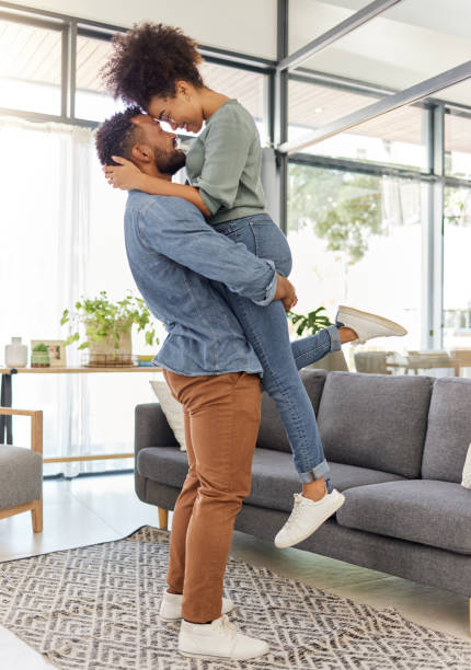 istock Happy mixed race couple hugging while relaxing at home. Content hispanic husband smiling and holding his wife while staring into her eyes lovingly and hugging in the lounge at home 1398982373