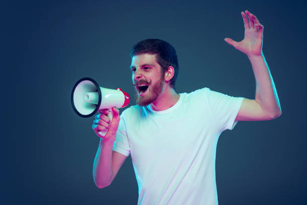 istock Guy shouting at megaphone. Handsome caucasian man's portrait isolated on dark blue studio background. 1398983384