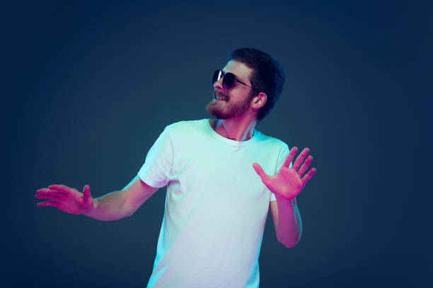 Nightlife. Stylish handsome man in white t-shirt dancing isolated on dark blue studio background. Concept of human emotions, facial expression, sales, ad, fashion and beauty