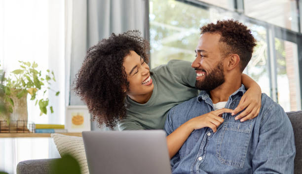 istock Mixed race couple smiling while using a laptop together at home. Cheerful hispanic boyfriend and girlfriend laughing while relaxing and using a laptop in the lounge at home 1398984262