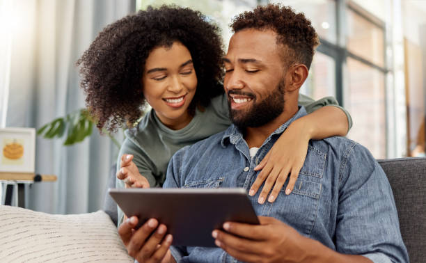 istock Mixed race couple smiling while using a digital tablet together at home. Cheerful hispanic boyfriend and girlfriend relaxing and using social media on a digital tablet in the lounge at home 1398984264