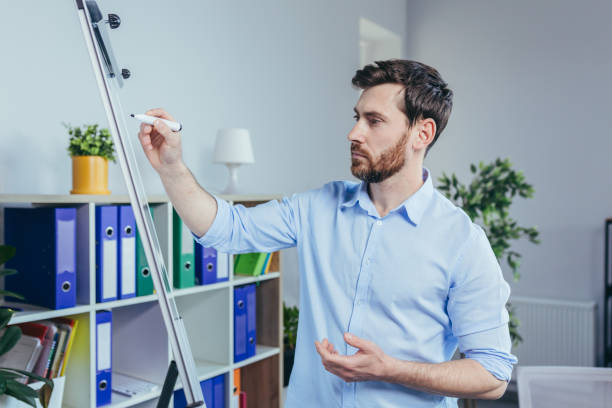 istock Young businessman writing on white board with marker business strategy plan, man working in modern bright office 1398988438