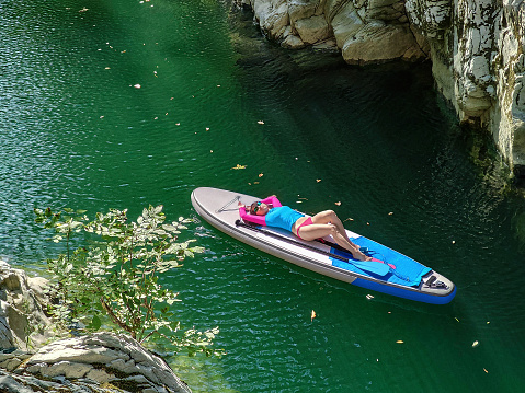Young woman lying and relaxing on stand-up paddle board on river water