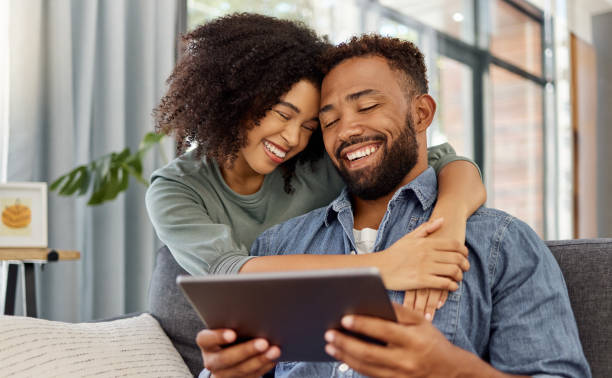 istock Happy young mixed race couple smiling while using a digital tablet together at home. Cheerful hispanic boyfriend and girlfriend laughing while bonding and using social media on a digital tablet in the lounge at home 1398989711