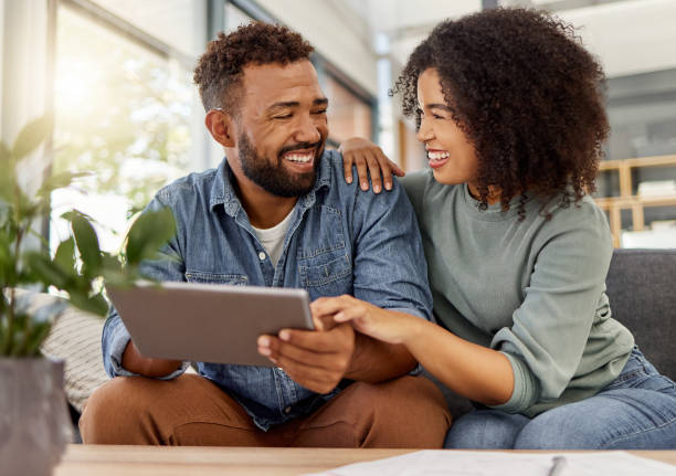 istock Happy young mixed race couple smiling while using a digital tablet together at home. Cheerful hispanic boyfriend and girlfriend laughing while relaxing and using social media on a digital tablet sitting on the couch in the lounge at home 1398990736