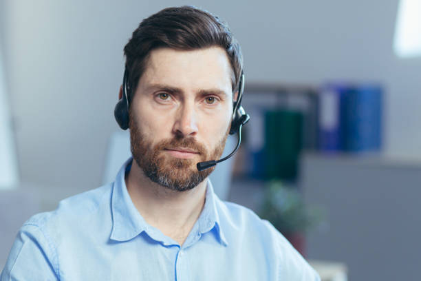 retrato de um técnico sério em uma loja, um homem olhando para a câmera pensativo usa um fone de ouvido para uma chamada de vídeo - portrait male pensive sofa - fotografias e filmes do acervo