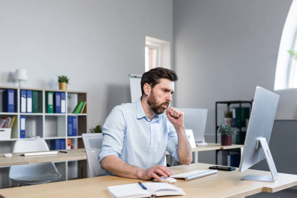 istock Sick and tired young man at work. Office worker, manager, freelancer sitting at a desk in the office does not feel well, wipes his nose, has a runny nose, coughs, headaches, holds his head. 1398991082