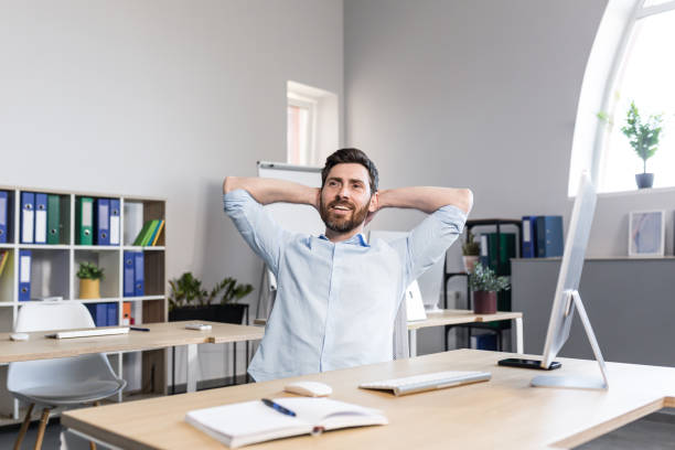 istock Young handsome man, office worker, sitting at a computer desk, stretching, tired, taking a break, doing yoga exercises, resting 1398991152