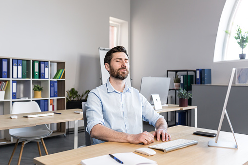 Businessman in the office with closed eyes performs breathing exercises, freelancer working on the computer