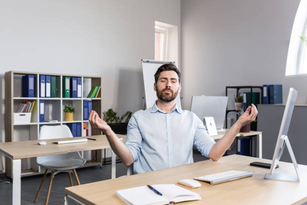 istock Young handsome man, office worker, sitting at a computer desk, stretching, tired, taking a break, doing yoga exercises, resting 1398991157