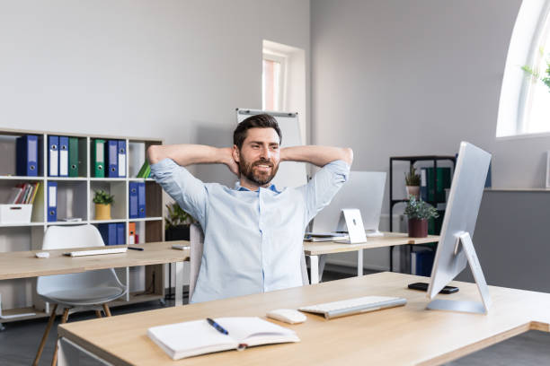 istock Young handsome man, office worker, sitting at a computer desk, stretching, tired, taking a break, doing yoga exercises, resting 1398991158