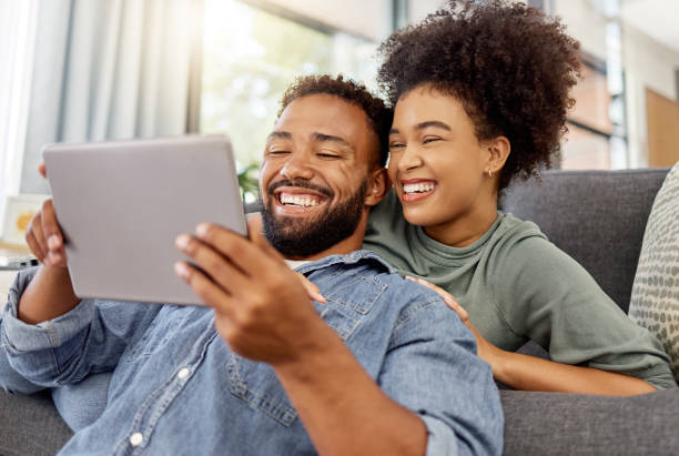 istock Mixed race couple smiling while using a digital tablet together at home. Joyful hispanic boyfriend and girlfriend laughing while relaxing and using social media on a digital tablet in the lounge at home 1398991233