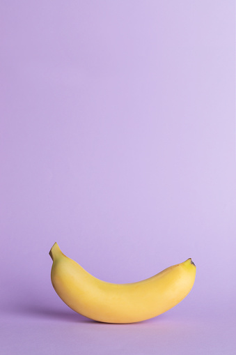 Single yellow banana on purple background.