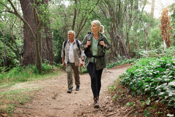 зрелая кавказская пара отправляется в поход вместе. пожилые мужчина и женщина улыбаются и гуляют по лесу на природе - пешеходный туризм стоковые фото и изображения