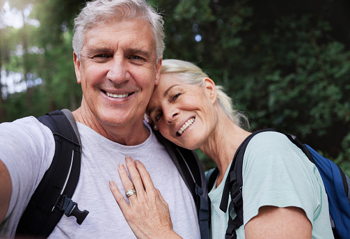 Portrait of a senior caucasian couple smiling and taking a selfie in a forest during a hike in the outdoors. Man and wife showing affection and holding each other during a break in nature