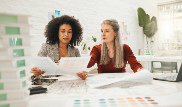 istock Two businesspeople collaborate on a project together. Team of designers reading documents together. Mature businesswoman working with her staff member. Boss working on a architectural project 1398994129