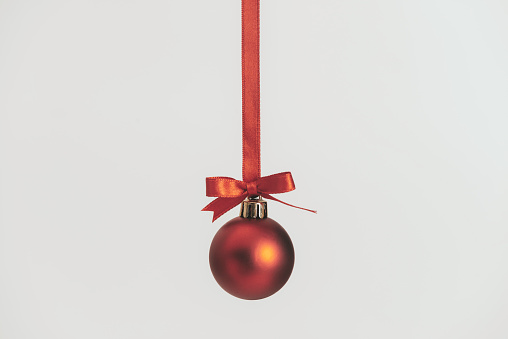 One red christmas bauble hanging with red ropes in front of white background