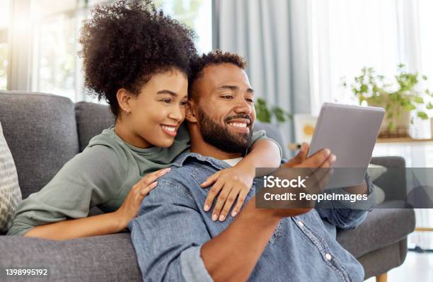 Mixed Race Couple Smiling While Using A Digital Tablet Together At Home Content Hispanic Boyfriend And Girlfriend Relaxing And Using Social Media On A Digital Tablet In The Lounge At Home Stock Photo - Download Image Now