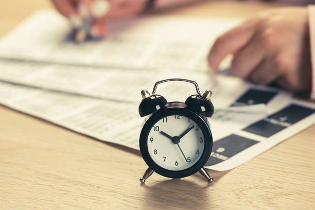 istock alarm clock with time running out. Students hands to take exams, write examination room with pencil holding on optical form of standardized test with answers 1398995651