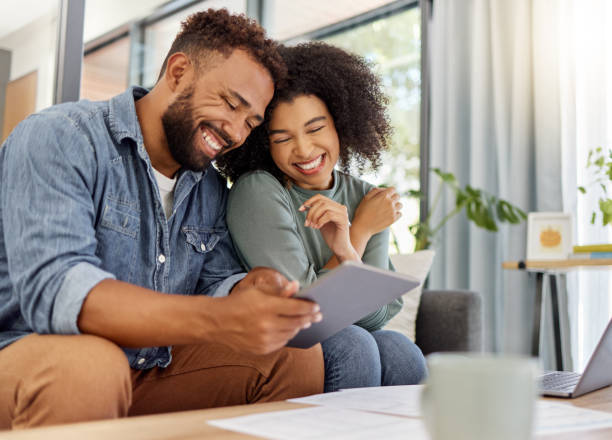 young happy mixed race couple going through documents and using a digital tablet at a table together at home. cheerful hispanic husband and wife smiling while planning and paying bills. boyfriend and girlfriend working on their budget - investering stockfoto's en -beelden