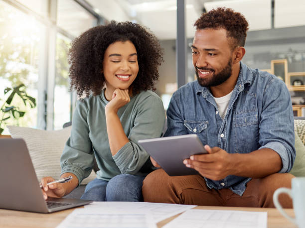 istock Young happy mixed race couple going through documents and using a digital tablet and laptop at a table together at home. Hispanic husband and wife smiling while planning and paying bills. Boyfriend and girlfriend working on their budget 1398995712