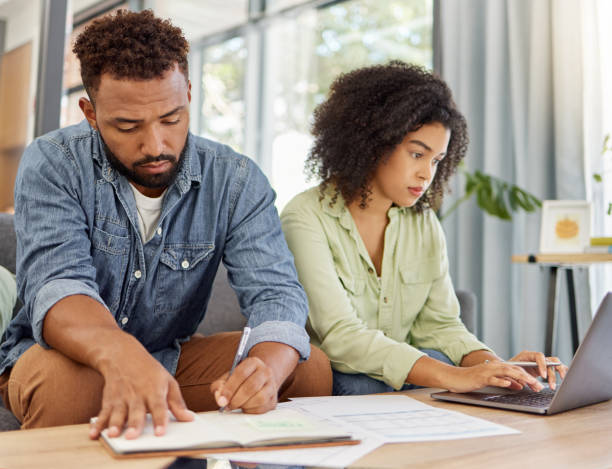 istock Young mixed race couple going through bills and using a laptop at a table together at home. Husband and wife planning and working on their finances together 1398995714