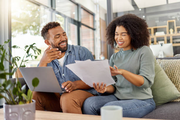istock Young happy mixed race couple going through documents and using a laptop at a table together at home. Cheerful hispanic husband and wife smiling while planning and paying bills. Boyfriend and girlfriend working on their budget 1398995755