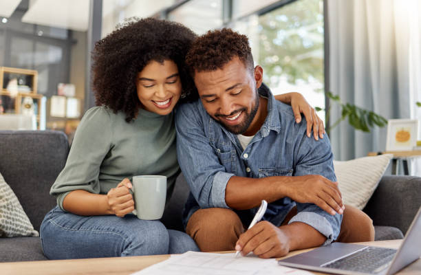 istock Young mixed race couple going through bills and using a laptop at a table together at home. Husband and wife planning and working on documents 1398995765