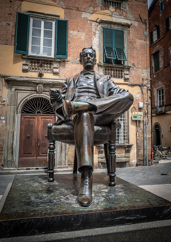 Luuca, Tuscany, Italy, 09 May 2022 - Statue of Giacomo Puccini inside Medieval city walls of Lucca, with old building with shuttered windows in the background.