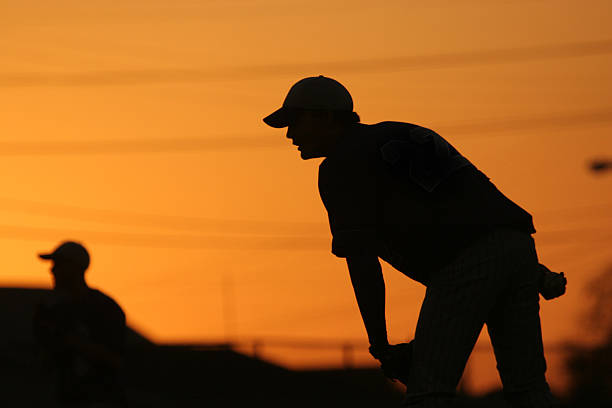 Silhouette of a baseball pitcher about to throw at sunset kid pitching baseball high school game baseball sport photos stock pictures, royalty-free photos & images