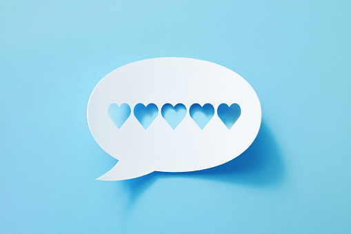 Circular white chat bubble with cut out heart symbols sitting on blue background. Horizontal composition with copy space.