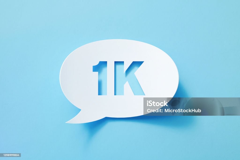 Circular White Chat Bubble With Cut Out 1K Symbol Sitting On Blue Background Circular white chat bubble with cut out 1K symbol sitting on blue background. Horizontal composition with copy space. Number 1000 Stock Photo