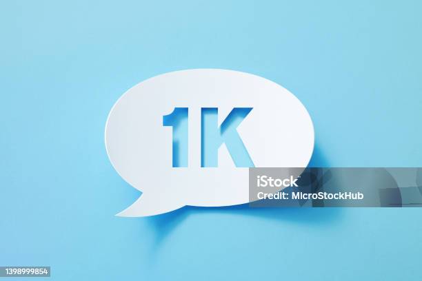 Circular White Chat Bubble With Cut Out 1k Symbol Sitting On Blue Background Stock Photo - Download Image Now