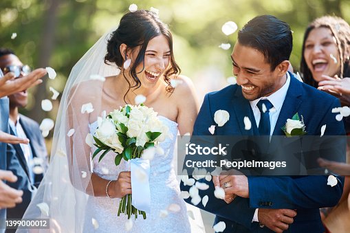istock Guests throwing confetti over bride and groom as they walk past after their wedding ceremony. Joyful young couple celebrating their wedding day 1399000012