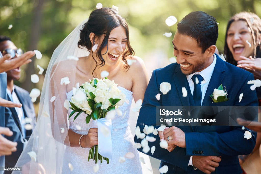 Guests throwing confetti over bride and groom as they walk past after their wedding ceremony. Joyful young couple celebrating their wedding day Wedding Stock Photo