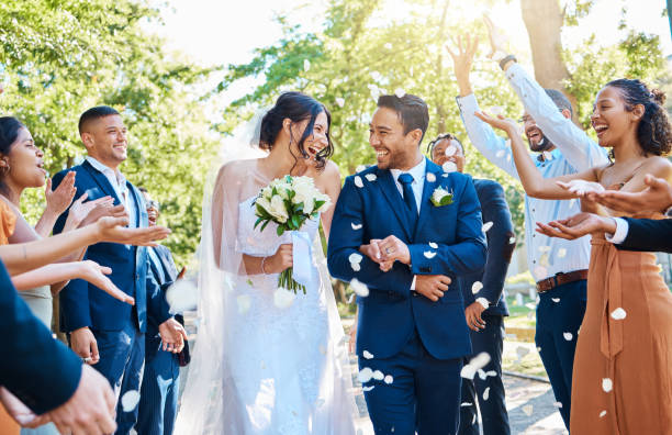 Wedding guests throwing rose petals confetti tradition over bride and groom on their special day. Newlywed couple walking past friends and family Wedding guests throwing rose petals confetti tradition over bride and groom on their special day. Newlywed couple walking past friends and family newlywed photos stock pictures, royalty-free photos & images