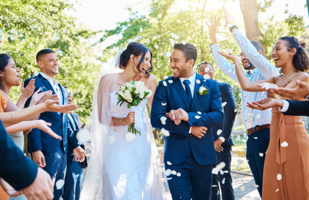 wedding guests throwing rose petals confetti tradition over bride and groom on their special day. newlywed couple walking past friends and family - newlywed imagens e fotografias de stock