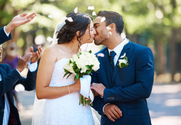 szczęśliwa para młoda dzieląca się pocałunkiem w otoczeniu gości i obsypywana płatkami róż konfetti po ceremonii ślubnej - weddings brown hair cheerful affectionate zdjęcia i obrazy z banku zdjęć
