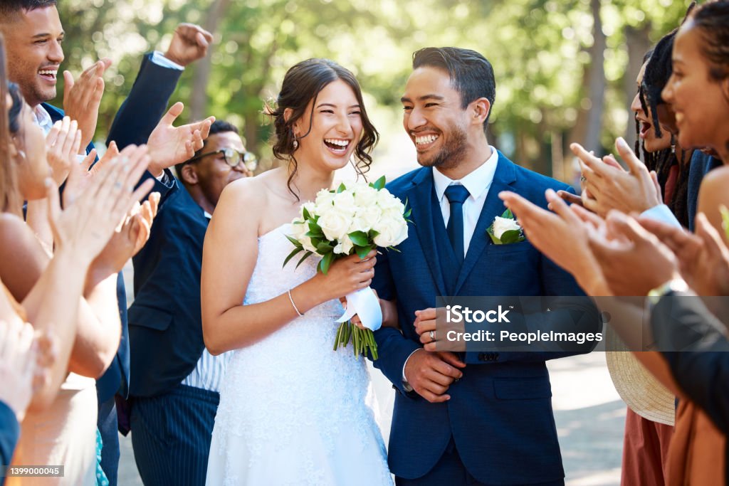 Wedding guests clapping hands as the newlywed couple walk down the aisle. Joyful bride and groom walking arm in arm after their wedding ceremony Wedding Stock Photo