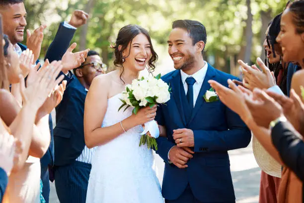 Photo of Wedding guests clapping hands as the newlywed couple walk down the aisle. Joyful bride and groom walking arm in arm after their wedding ceremony