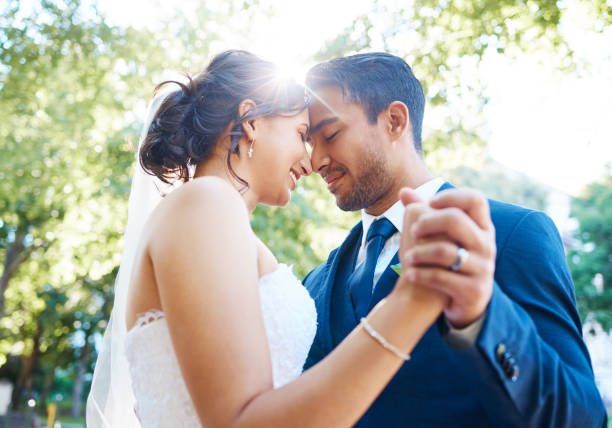 istock Bride and groom holding hands and touching foreheads while dancing outside. Mixed race newlyweds enjoying romantic moments on their wedding day. Happy young romantic couple sharing their first wedding dance 1399000162